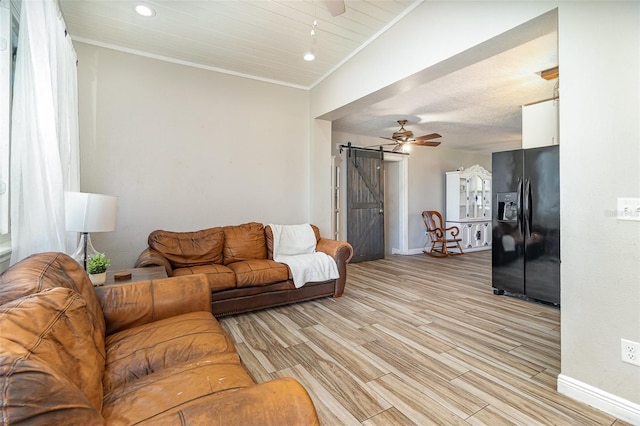 living room with light wood-type flooring, a barn door, baseboards, and a ceiling fan