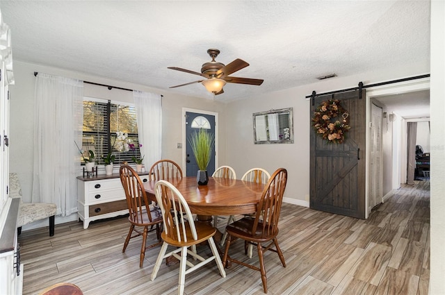 dining room featuring a barn door, light wood-style floors, a ceiling fan, and a textured ceiling