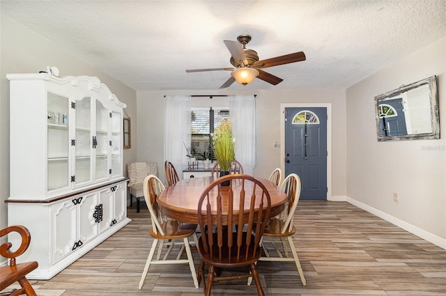 dining space featuring a textured ceiling, a ceiling fan, baseboards, and wood finish floors