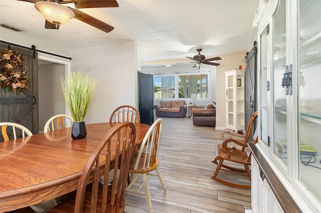 dining room with visible vents, wood finish floors, a ceiling fan, and a barn door