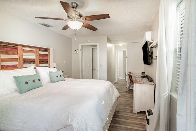 bedroom with visible vents, ceiling fan, a wall unit AC, wood finished floors, and a textured ceiling