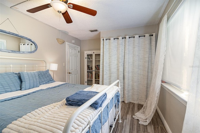 bedroom with visible vents, a ceiling fan, a textured ceiling, wood finished floors, and baseboards