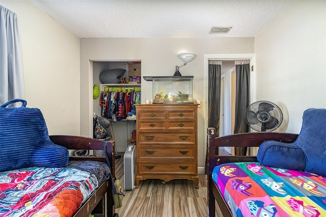 bedroom with a closet, visible vents, a textured ceiling, and wood finished floors