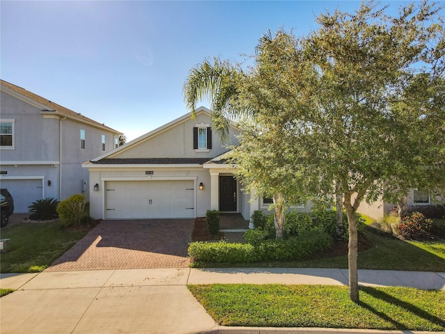 view of front facade featuring decorative driveway, a garage, a front lawn, and stucco siding