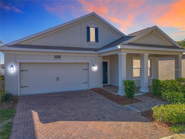 view of front facade with roof with shingles, a porch, an attached garage, stucco siding, and decorative driveway