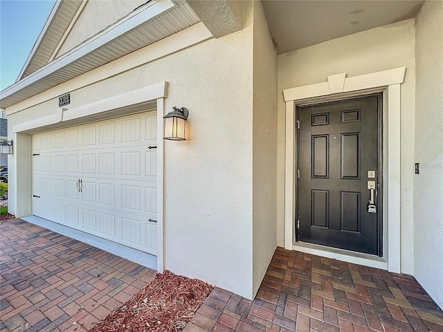 entrance to property featuring a garage and stucco siding