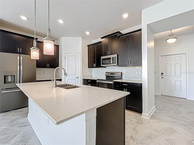 kitchen featuring tasteful backsplash, decorative light fixtures, an island with sink, stainless steel appliances, and a sink