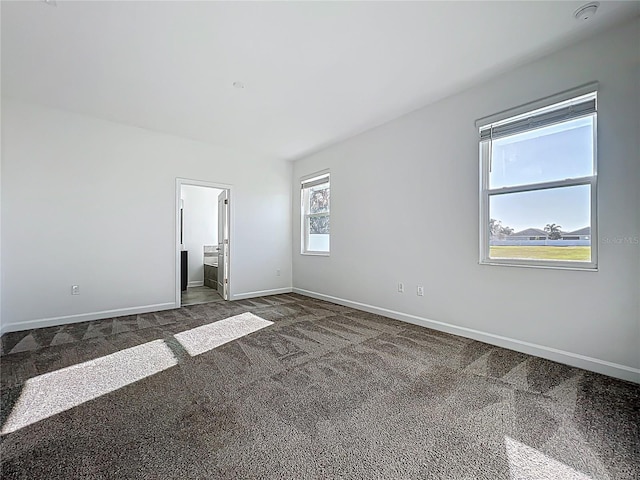 spare room with baseboards and dark colored carpet