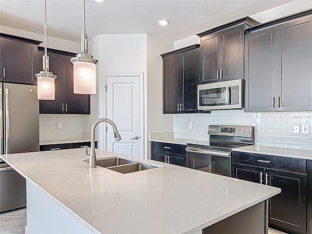 kitchen featuring tasteful backsplash, a center island with sink, pendant lighting, stainless steel appliances, and a sink