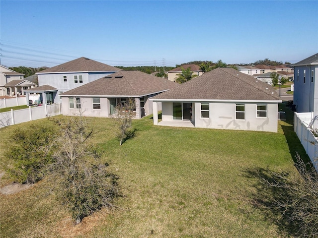 rear view of house with a fenced backyard, stucco siding, a shingled roof, and a yard