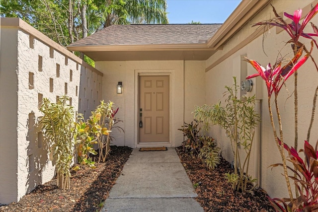 view of exterior entry with stucco siding and a shingled roof