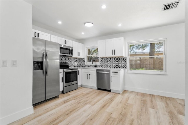 kitchen featuring visible vents, decorative backsplash, light wood-style flooring, white cabinets, and stainless steel appliances