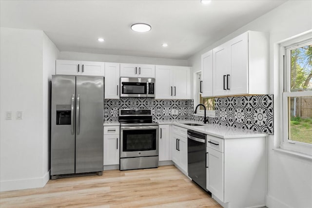 kitchen with tasteful backsplash, light wood finished floors, white cabinets, stainless steel appliances, and a sink