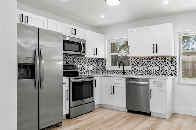 kitchen featuring light wood-type flooring, decorative backsplash, appliances with stainless steel finishes, and white cabinetry