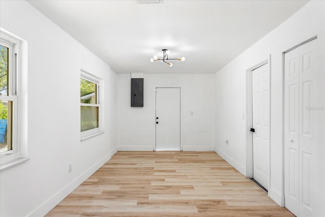 unfurnished room featuring electric panel, baseboards, light wood-style floors, and an inviting chandelier