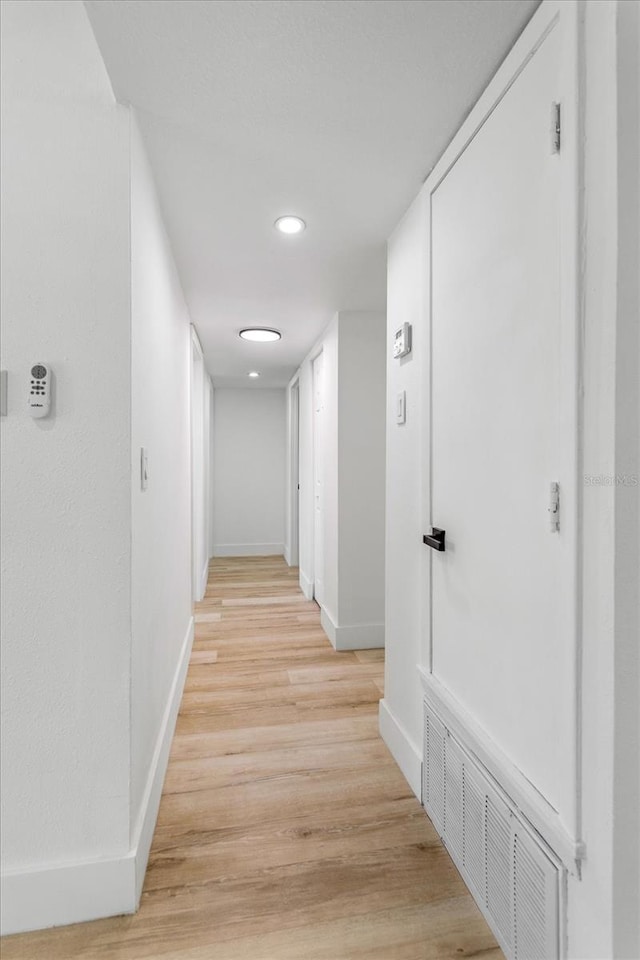 hallway with light wood-style floors, visible vents, and baseboards