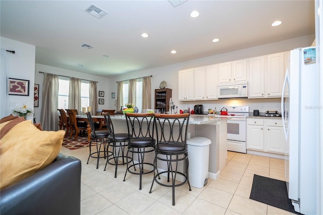 kitchen featuring visible vents, white appliances, open floor plan, and a kitchen breakfast bar