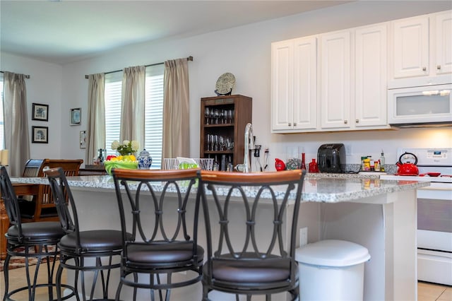 kitchen with a kitchen bar, white appliances, white cabinets, and light stone countertops