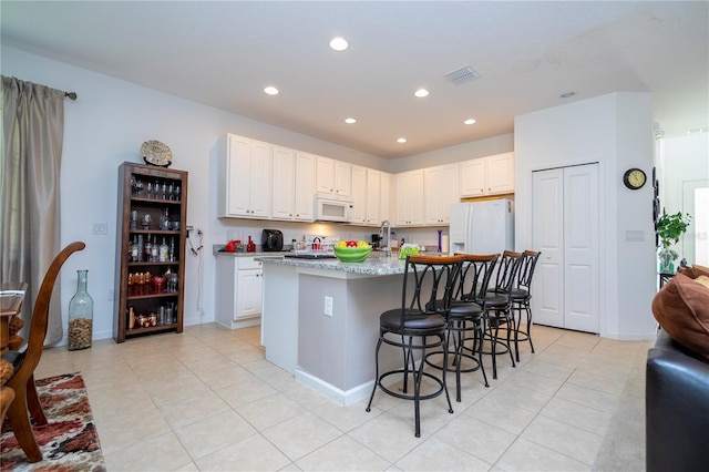 kitchen featuring white appliances, visible vents, a breakfast bar, recessed lighting, and white cabinets