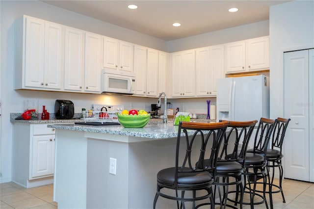 kitchen featuring a center island with sink, a breakfast bar, light tile patterned floors, white appliances, and white cabinetry