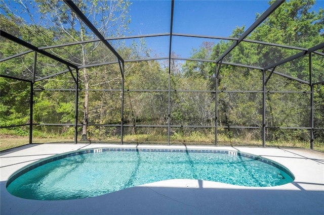 pool with a forest view, glass enclosure, and a patio area