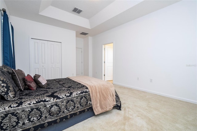 carpeted bedroom with a closet, visible vents, baseboards, and a tray ceiling
