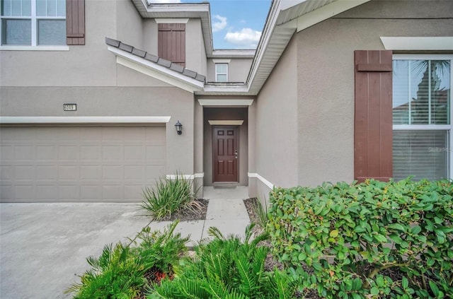 view of exterior entry with a garage, driveway, and stucco siding