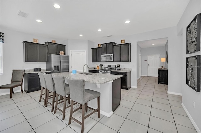 kitchen with a sink, a breakfast bar area, recessed lighting, appliances with stainless steel finishes, and a kitchen island with sink