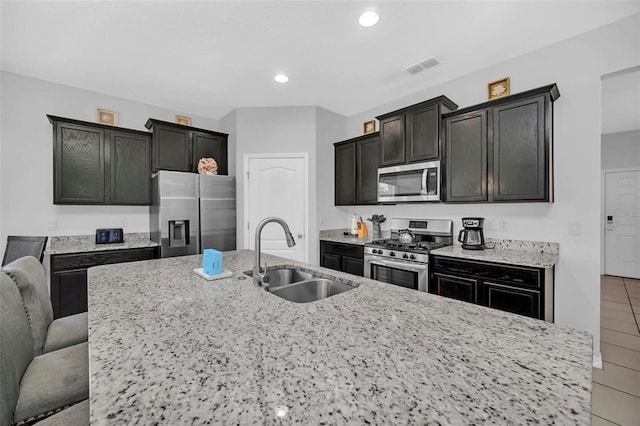 kitchen featuring visible vents, an island with sink, light stone counters, appliances with stainless steel finishes, and a sink