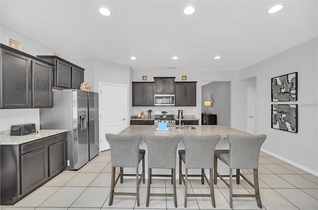 kitchen featuring a sink, light stone counters, a kitchen breakfast bar, appliances with stainless steel finishes, and light tile patterned flooring