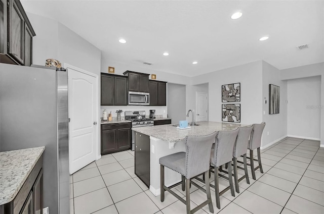 kitchen featuring visible vents, a center island with sink, stainless steel appliances, a breakfast bar area, and light tile patterned floors