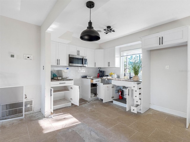 kitchen with a sink, stainless steel microwave, tasteful backsplash, white cabinetry, and hanging light fixtures