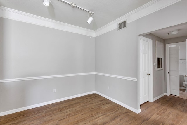 unfurnished room featuring visible vents, baseboards, wood finished floors, and ornamental molding