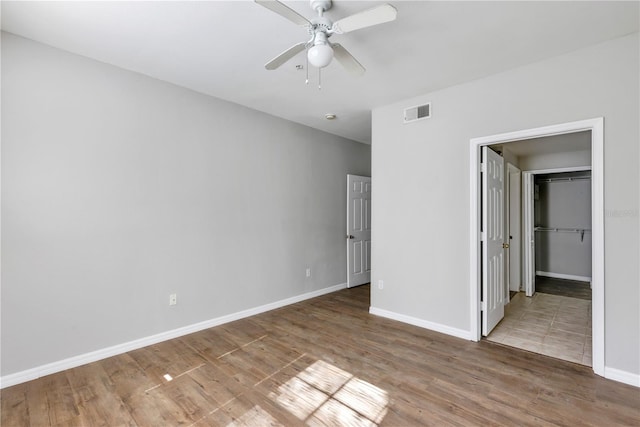 unfurnished bedroom featuring wood finished floors, visible vents, baseboards, ceiling fan, and a walk in closet