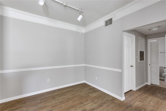 spare room featuring visible vents, track lighting, crown molding, baseboards, and wood finished floors