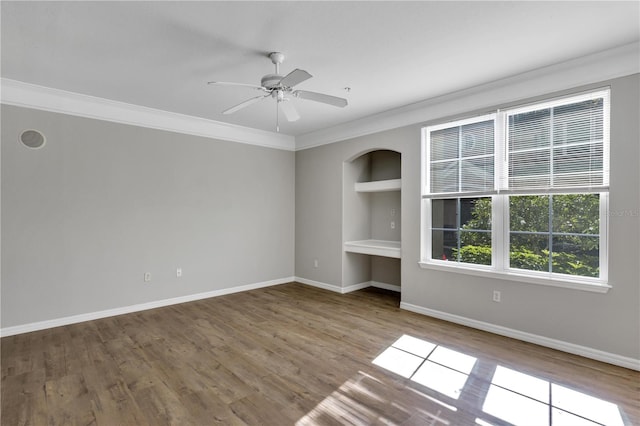 empty room featuring built in features, ornamental molding, baseboards, and wood finished floors