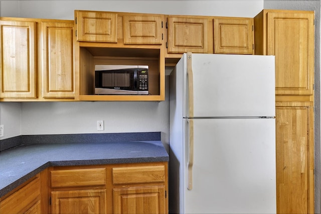 kitchen featuring dark countertops, stainless steel microwave, and freestanding refrigerator