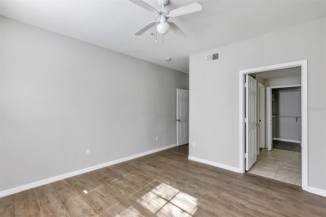 unfurnished bedroom with a spacious closet, visible vents, baseboards, wood finished floors, and a ceiling fan