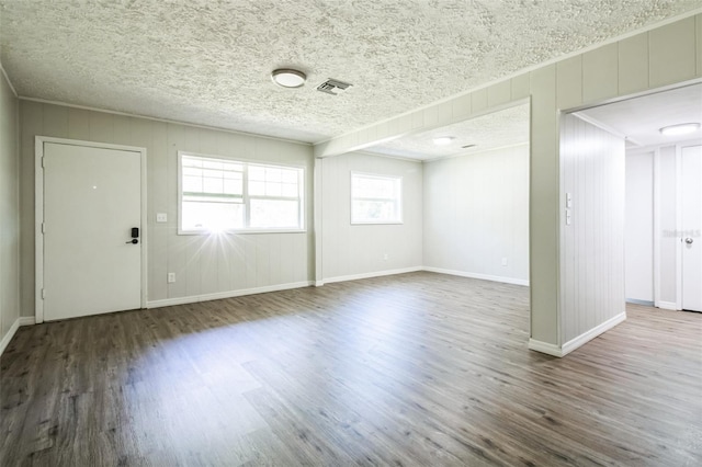 interior space featuring visible vents, a textured ceiling, baseboards, and wood finished floors