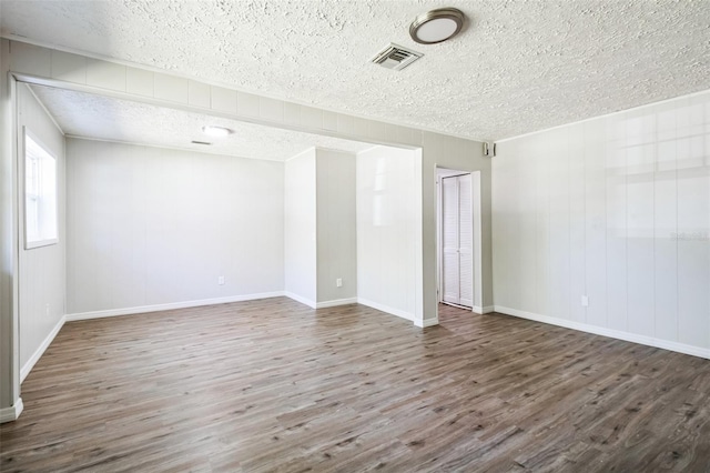 empty room with visible vents, baseboards, a textured ceiling, and wood finished floors