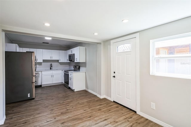 kitchen with wood finished floors, recessed lighting, stainless steel appliances, light countertops, and white cabinets