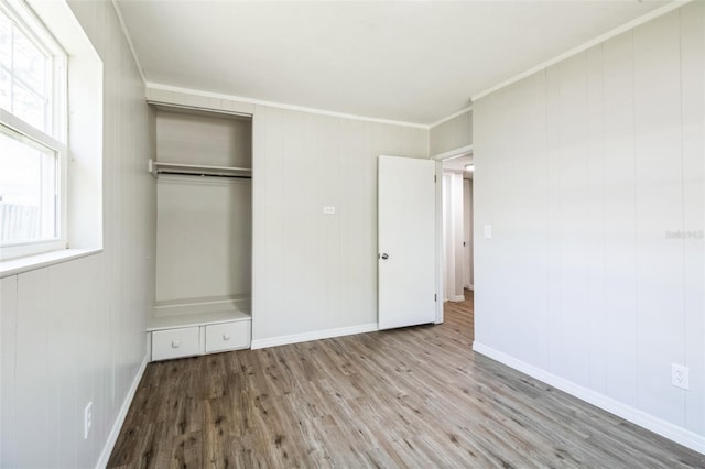 unfurnished bedroom featuring crown molding, wood finished floors, a closet, and baseboards