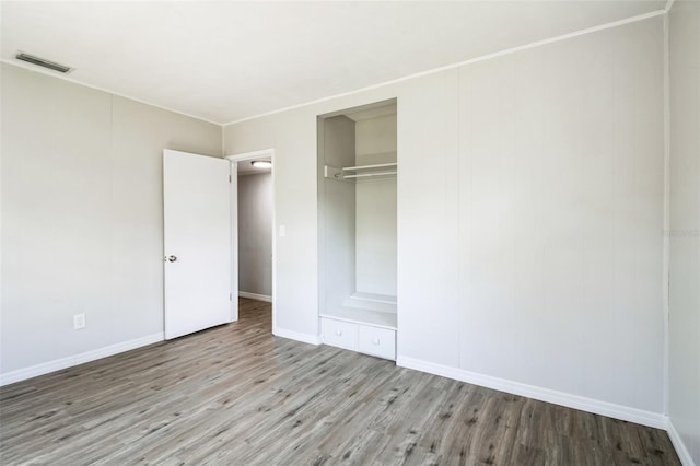 unfurnished bedroom featuring wood finished floors, visible vents, a closet, and baseboards