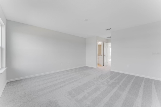 spare room featuring light colored carpet, visible vents, and baseboards