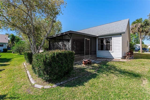 back of property with a lawn, a shingled roof, and a sunroom