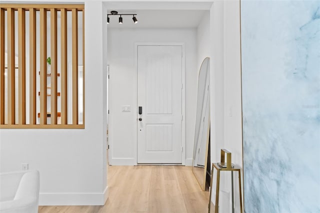 corridor featuring light wood-style flooring, rail lighting, and baseboards