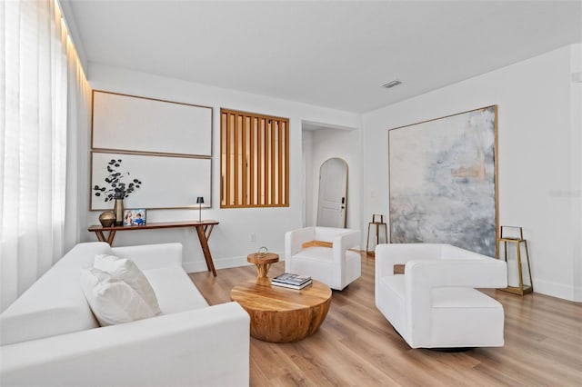 living room with arched walkways, visible vents, light wood-type flooring, and baseboards