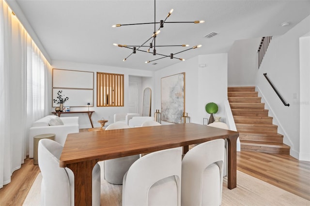 dining space with visible vents, light wood-style flooring, stairway, and an inviting chandelier