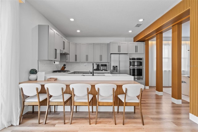 kitchen featuring a breakfast bar area, visible vents, a peninsula, light countertops, and appliances with stainless steel finishes