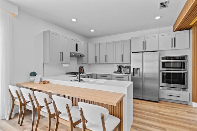 kitchen with visible vents, under cabinet range hood, stainless steel appliances, a peninsula, and light countertops